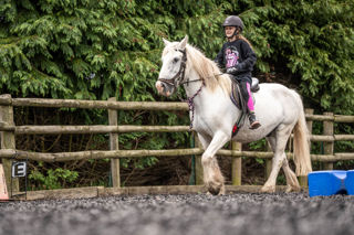An image of a girl riding a small white horse around Cantref Riding Centre's training area.