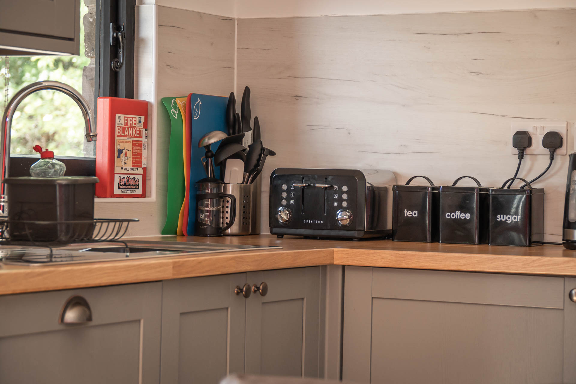 A close up image of a bright kitchen area with smart grey cabinets and wooden worksurface. There's a window above the sink which looks out onto the veranda.