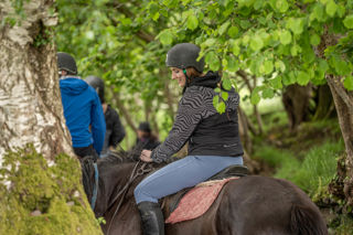 An image of a rider on a horse going through a low canopy pathway.