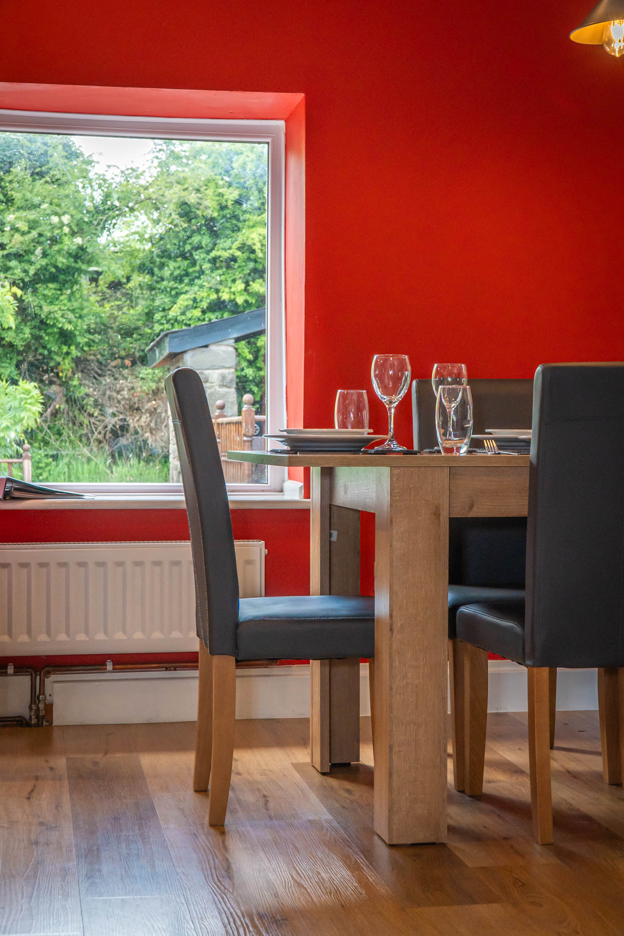 A image of a set dining table in front of a red feature wall and large window.