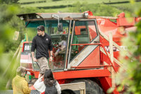 An image of a child sitting in the cab of a red combine harvester, pretending to drive it, whilst family watch on from outside.