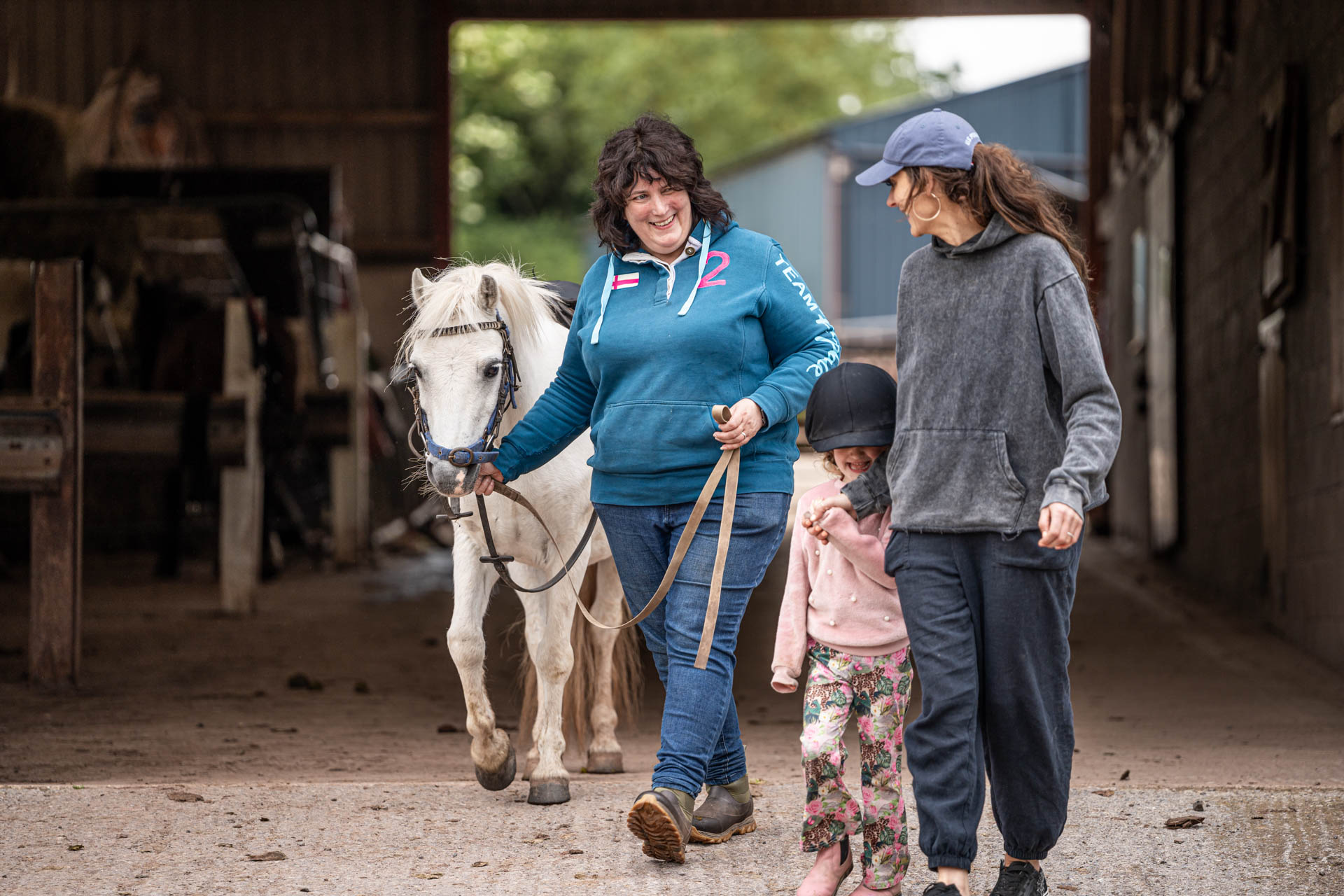 An image of a member of the Cantref team bringing a white pony out the stable for a young girl.