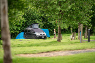 An image of a black VW campervan on a luscious, green pitch at Cantref Holidays.
