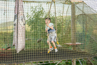 An image of a boy bouncing on a netted trampoline, holding onto a rope.