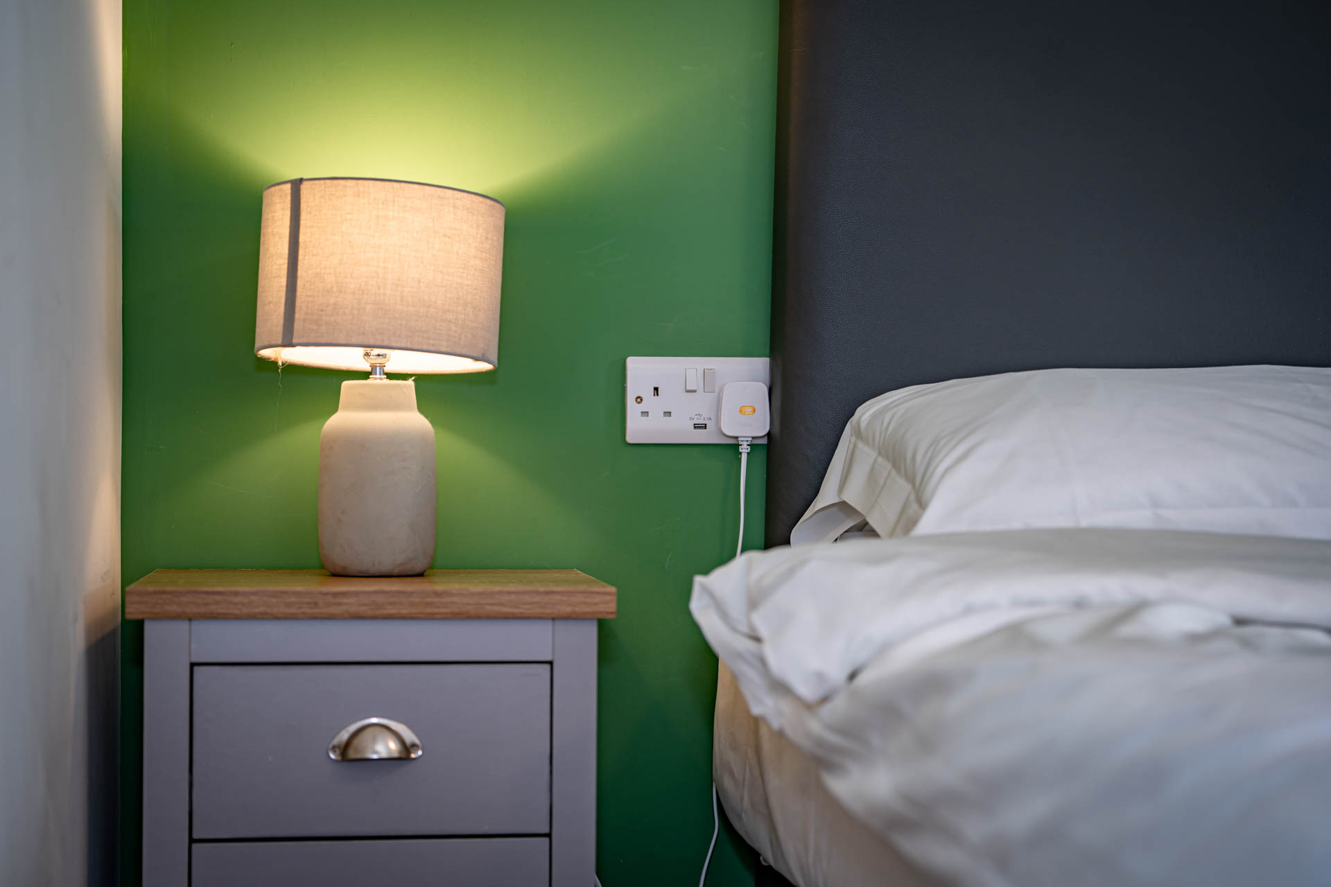 A close up image of a bedside table, lamp and bed.