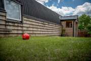 An image of a football on a small lawned area for outdoor games, next to a hayloft with a tin Barrell Vault roof and exterior wooden cladding.