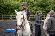 An image of a girl smiling on horseback whilst her sister gets her stirrups altered.