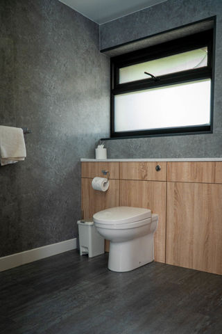 An image of a spacious family bathroom with frosted window, grey stone effect walls and dark grey wood effect flooring.