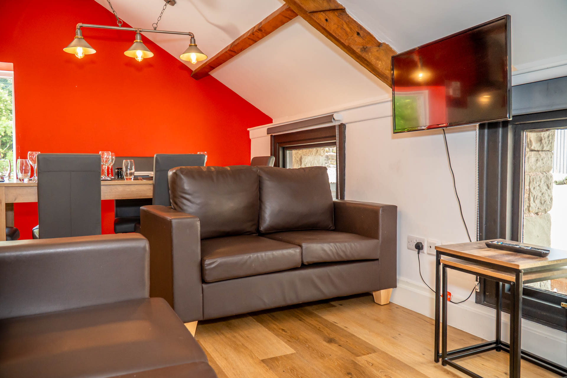 An image of The Milking Parlour's dining and living area, with red feature wall, leather chairs and sofas, Eddison bulb lighting and lots of natural light. 